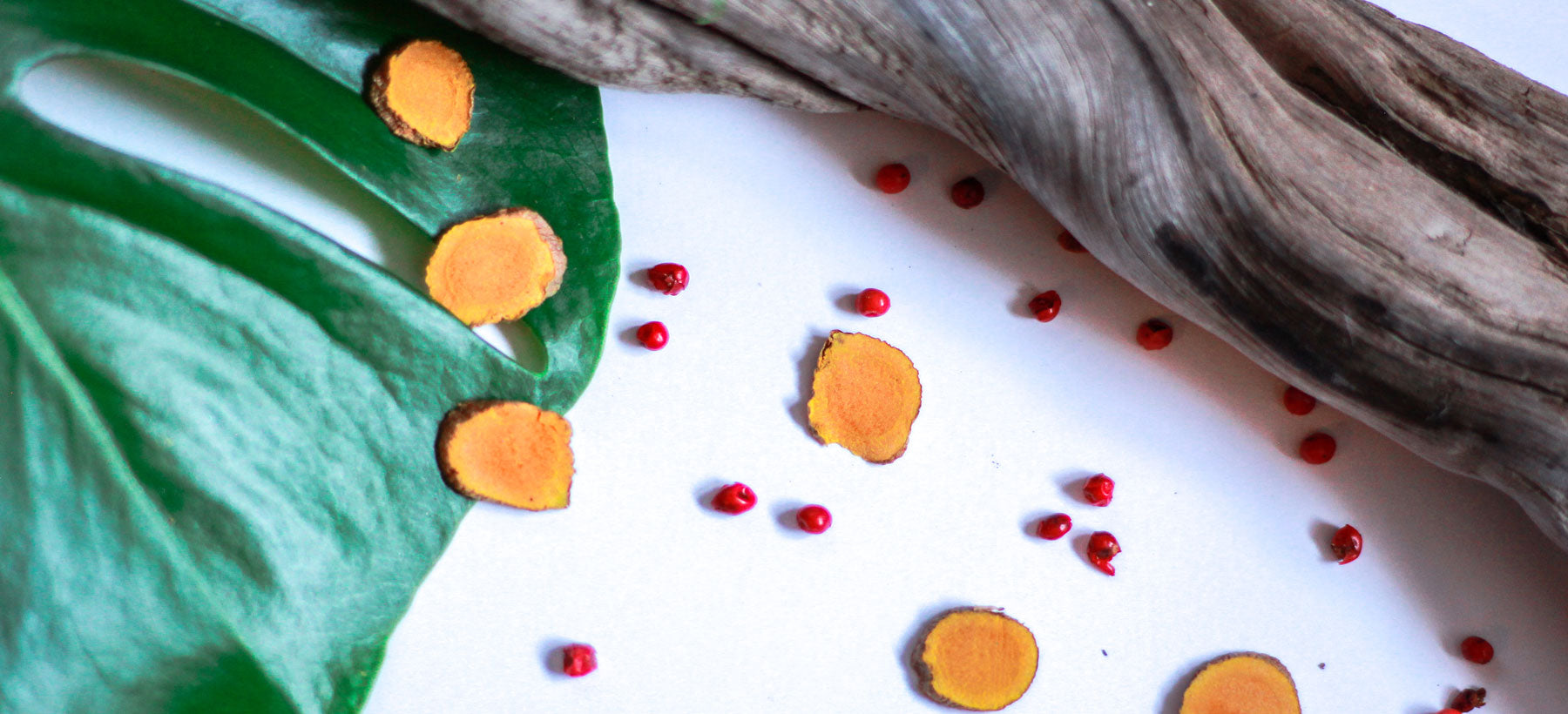 Turmeric slices and red seeds sprinkled next to a leaf and wooden branch